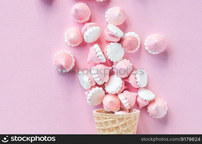 Multicolored pink and white meringues in waffle cookies lie scattered on a pink background. Colorful bright meringues in waffle cookies lie on a pink background