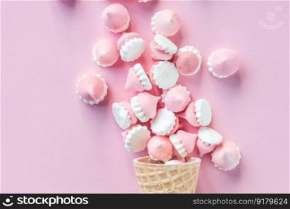 Multicolored pink and white meringues in waffle cookies lie scattered on a pink background. Colorful bright meringues in waffle cookies lie on a pink background