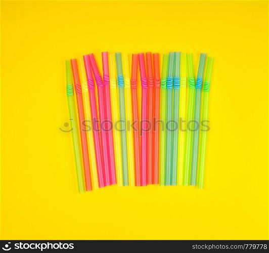 multicolored plastic cocktail tubes on a yellow background, flat lay