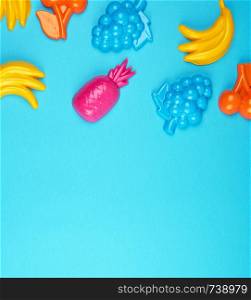 multicolored plastic toys fruits on a blue background, close up