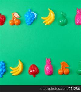 multicolored plastic toys fruits on a green background, copy space