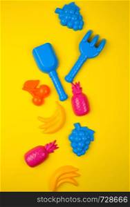 multicolored plastic toys fruits on a yellow background, close up