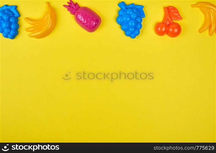 multicolored plastic toys fruits on a yellow background, copy space