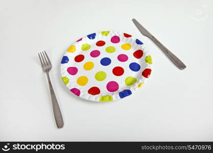 Multicolored plate with polka dots and cutlery over white background
