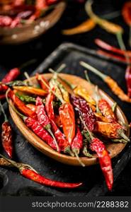 Multicolored pods of dried chili peppers on a cutting board. On a black background. High quality photo. Multicolored pods of dried chili peppers on a cutting board.