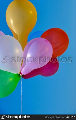 Multicolored rubber balloons fly up against a blue clear sky