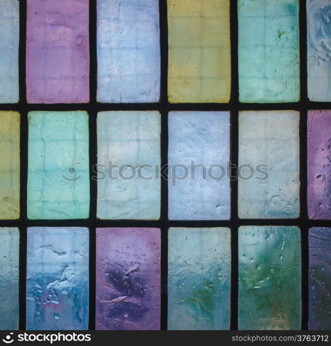 multicolored stained glass window with regular block pattern in hue of blue green violet, square format