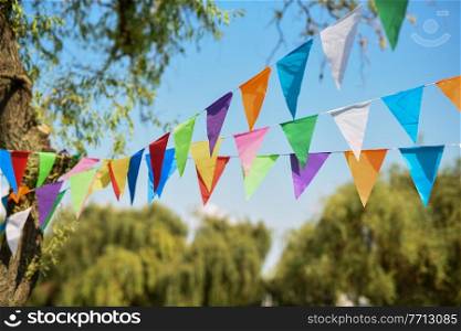 multicolored triangular decoration flags are stretched between trees