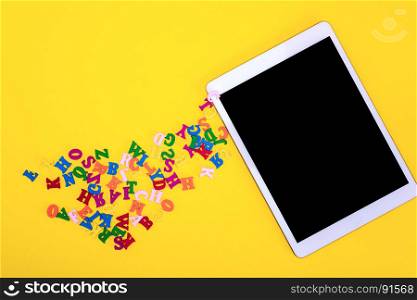 multicolored wooden letters and electronic tablet with a black screen on a yellow background