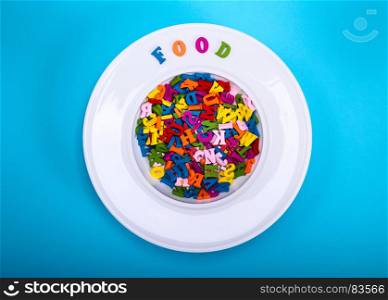 multicolored wooden letters in white ceramic plate for soup, near word food, blue background, top view