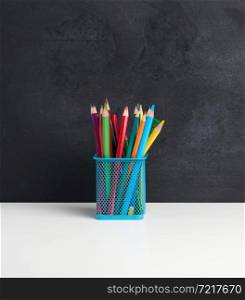 multicolored wooden pencils in a metal basket on a black chalk board background