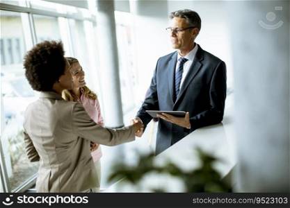 Multiethnic business people using digital tablet while standing and handshaking in the modern office