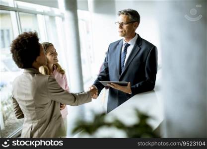 Multiethnic business people using digital tablet while standing and handshaking in the modern office