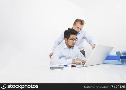 Multiethnic businessmen working on laptop at desk in office