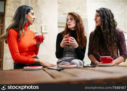 Multiethnic group of three happy female friends drinking coffee in a cafe bar.. Group of three happy friends drinking coffee in a cafe bar.