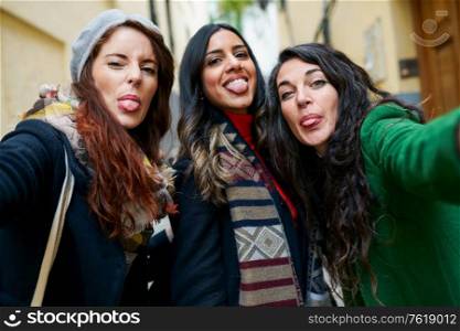 Multiethnic group of woman taking a selfie photo sticking out their tongues outdoors. Group of woman taking a selfie photo sticking out their tongues