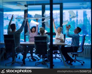 multiethnic Group of young business people throwing documents and looking happy while celebrating success at their working places in night office