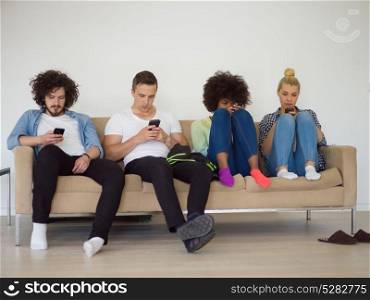 multiethnic group of young people sitting on a sofa at home,staring at smartphone, being antisocial, smartphone addiction