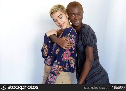 Multiethnic joyful women embrace and enjoy togetherness while looking at camera against background.