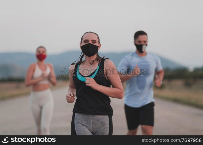 Multiethnic runners group wear face masks running keep social distance outdoor. Fit healthy diverse team wears sportswear jogging in the evening on nature sports track distancing for safety.. Multiethnic runners group wear face masks running keep social distance outdoor. Fit healthy diverse team wears sportswear jogging in evening on nature sports track distancing for safety.