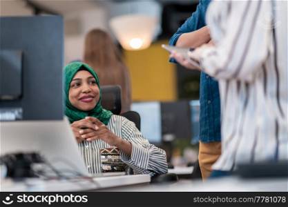 Multiethnic startup business team Arabian woman wearing a hijab on meeting in modern open plan office interior brainstorming, working on laptop and desktop computer. Selective focus. High-quality photo. Multiethnic startup business team Arabian woman wearing a hijab on meeting in modern open plan office interior brainstorming, working on laptop and desktop computer. Selective focus