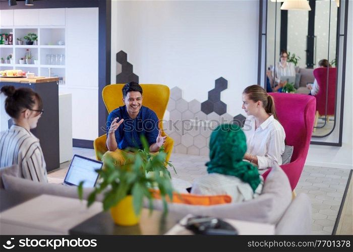 Multiethnic startup business team having brainstorming in relaxation area of modern office interior working on laptop and tablet computer