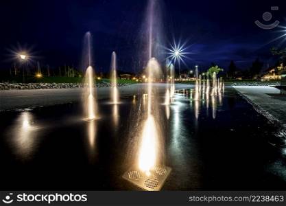 Multiple jets of water in a fountain, lighting show on ground in night time at city square