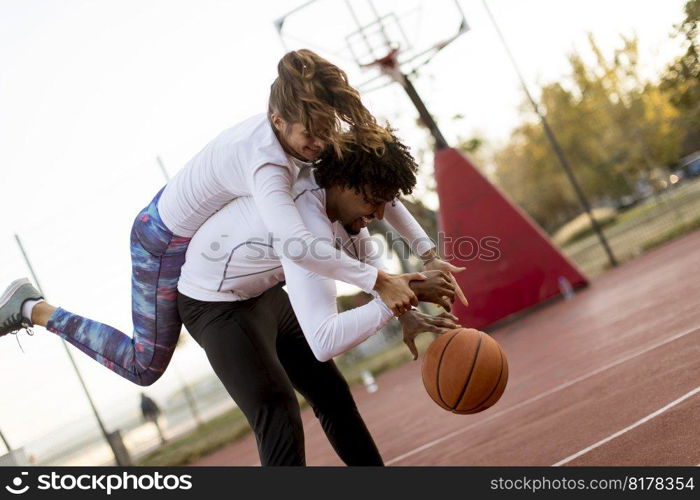 Multiracial couple playing basketball at court