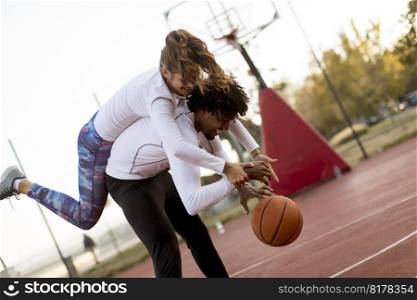 Multiracial couple playing basketball at court