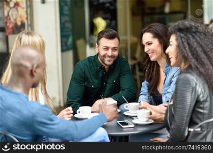 Multiracial group of five friends having a coffee together. Three women and two men at cafe, talking, laughing and enjoying their time. Lifestyle and friendship concepts with real people models. Multiracial group of five friends having a coffee together