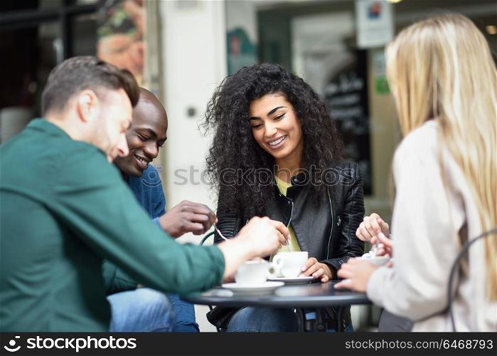 Multiracial group of four friends having a coffee together. Two women and and two men at cafe, talking, laughing and enjoying their time.
