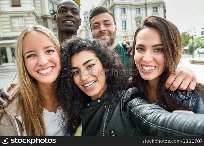 Multiracial group of friends taking selfie in a urban street with a muslim woman in foreground. Three young women and two men wearing casual clothes.