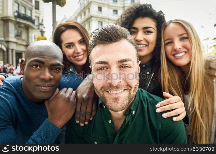 Multiracial group of friends taking selfie in a urban street with a caucasian man in foreground. Three young women and two men wearing casual clothes.