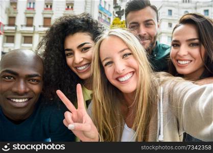 Multiracial group of friends taking selfie in a urban street with a blonde woman in foreground. Three young women and two men wearing casual clothes.. Multiracial group of young people taking selfie