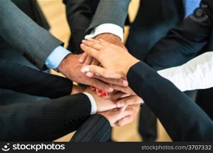 Multiracial group of nine diverse businesspeople standing in a circle facing each other joining hands in a team