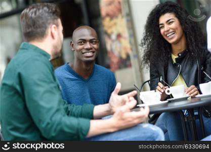 Multiracial group of three friends having a coffee together. A woman and two men at cafe, talking, laughing and enjoying their time. Lifestyle and friendship concepts with real people models