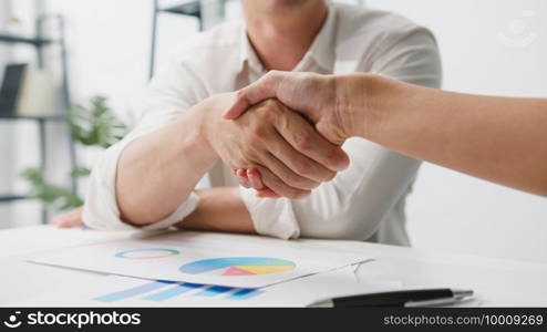 Multiracial group of young creative people in smart casual wear discussing business shaking hands together and smiling while sitting in modern office. Partner cooperation, coworker teamwork concept.