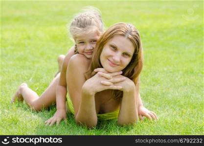 Mum and daughter lie on a green lawn in a bikini and look in the frame