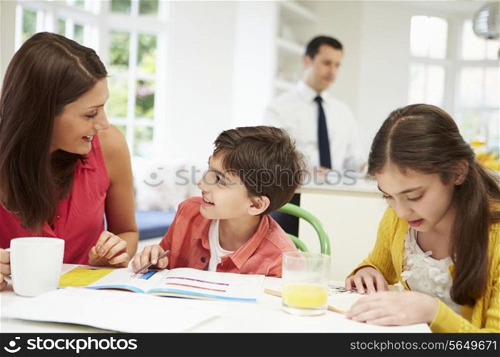 Mum Helps Children With Homework As Dad Works In Background