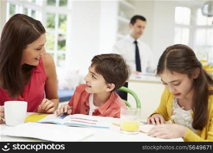 Mum Helps Children With Homework As Dad Works In Background