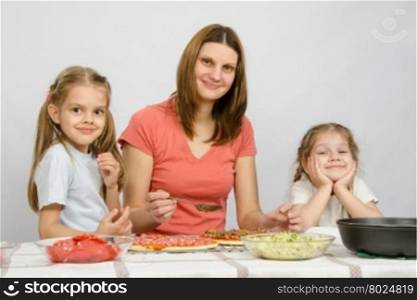 Mum with two little girls sitting at the kitchen table preparing a pizza