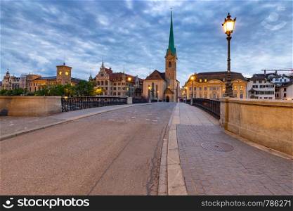 Munsterbrucke bridge and the bell tower of the Fraumunster church at sunset.. Zurich. City embankment and the Munsterbrucke bridge at sunset.