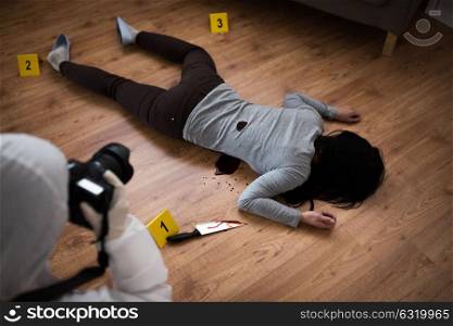 murder, investigation and forensic examination concept - criminalist with camera photographing dead female victim body at crime scene (staged photo). criminalist photographing dead body at crime scene