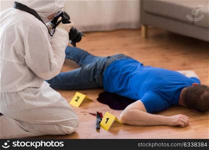 murder, investigation and forensic examination concept - criminalist with camera photographing dead male victim body at crime scene (staged photo). criminalist photographing dead body at crime scene