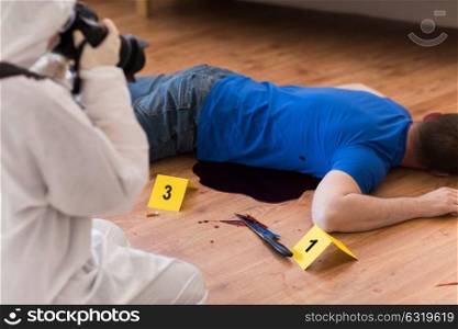 murder, investigation, forensic examination and people concept - criminalist with camera photographing dead male victim body at crime scene. criminalist photographing dead body at crime scene