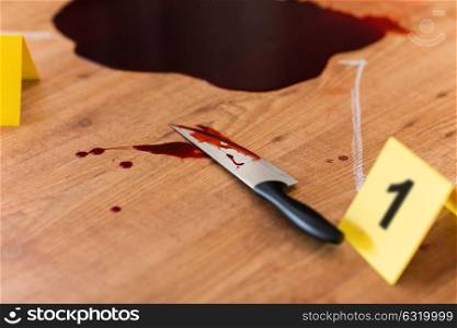 murder, kill and forensic evidence concept - knife in blood lying on floor near chalk outline of body at crime scene. knife in blood and chalk outline at crime scene