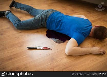 murder, kill and people concept - dead man body and knife in blood lying on floor at crime scene (staged photo). dead man body lying on floor at crime scene