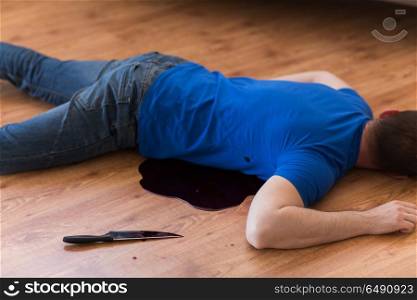 murder, kill and people concept - dead man body and knife in blood lying on floor at crime scene (staged photo). dead man body lying on floor at crime scene. dead man body lying on floor at crime scene