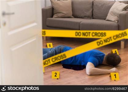 murder, kill and people concept - dead man body in blood lying on floor and bullet sleeves fenced by police tape at crime scene at home room. dead man body in blood on floor at crime scene