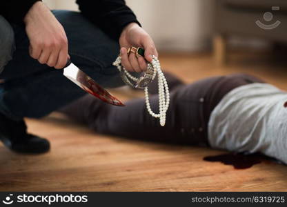 murder, robbery and people concept - criminal or murderer holding knife in blood and jewelry and dead woman body lying on floor at crime scene. criminal with knife and jewelry at crime scene